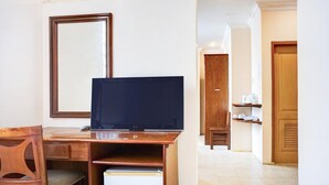 Habitación de hotel con un escritorio de madera, un televisor, un espejo y una puerta que da a un pasillo.