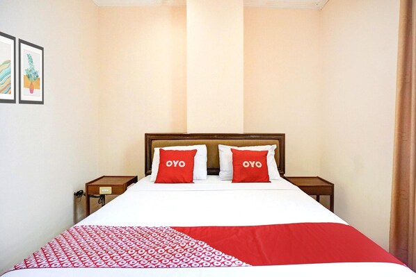 A hotel room with a bed, two pillows with 'OYO' text, a bedside table, and a wall-mounted artwork.
