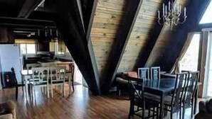 Un comedor con piso de madera, una araña y vista a la cocina.