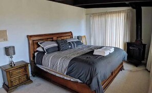 A bedroom with a wooden bed, a nightstand, a lamp, and a fireplace. - Top of the Mountain Lodge (South Lake Tahoe)