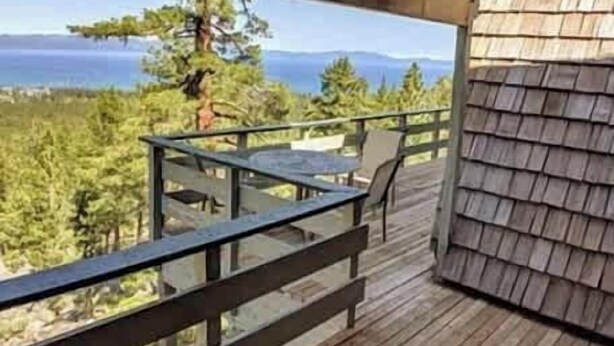 Una terraza de madera con una mesa y sillas, con vistas a un bosque y una masa de agua.