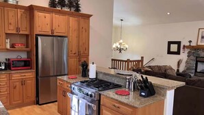 A kitchen with wooden cabinets, a stainless steel refrigerator, a gas stove, and a granite countertop. - Upscale Mountain home on the bike path (South Lake Tahoe)