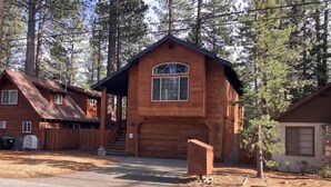 A two-story wooden cabin with a garage, a covered porch, and a driveway. - Upscale Mountain home on the bike path (South Lake Tahoe)