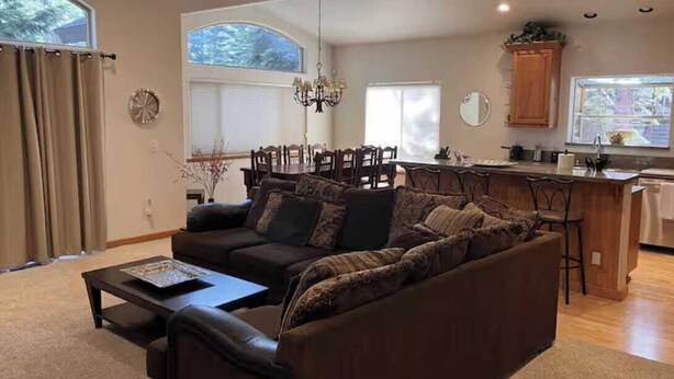 A living room with a sofa, coffee table, dining area with chairs, kitchen area, and large windows. - Upscale Mountain home on the bike path (South Lake Tahoe)