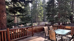 A wooden deck with a table and chairs, surrounded by tall trees. - Upscale Mountain home on the bike path (South Lake Tahoe)