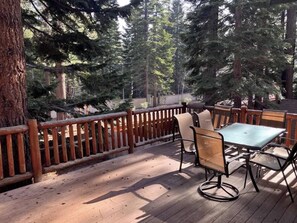 Eine Holzterrasse mit Tisch und Stühlen, umgeben von hohen Bäumen.
