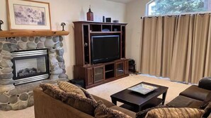 A living room with a stone fireplace, a television, a sofa, and a window with curtains. - Upscale Mountain home on the bike path (South Lake Tahoe)