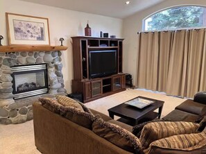 Ein Wohnzimmer mit Kamin aus Stein, einem Fernseher, einer Couch und einem Fenster mit Vorhängen.