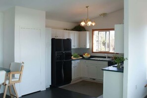 A modern kitchen with white cabinets, a black refrigerator, and a dining area with a wooden chair.