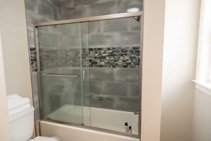 A bathroom with a glass-enclosed shower, a white toilet, and a tiled backsplash.