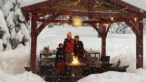 Ett snötäckt utomhusområde med en träkonstruktion, eventuellt en pergola, och en eldstad.