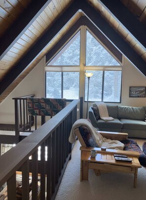 Ein gemütliches Schlafzimmer im Loft-Stil mit schrägem Dach, großen Fenstern, einem Balkon, einer Couch und einem Couchtisch.