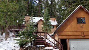 A wooden cabin with a stone staircase, a garage, and a forested backdrop. - Cabin close to hiking trails and ski resorts (South Lake Tahoe)