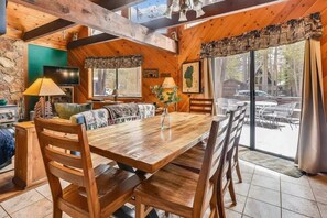 Un interior de madera con una mesa de comedor, sillas, un sofá, un televisor y una ventana con vistas al exterior.