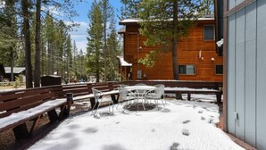 Un edificio in legno con una zona salotto all'aperto coperta, circondato da alberi.