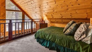 Una camera da letto con soffitto spiovente, un letto con lenzuola verdi, un comodino e una finestra vista foresta.