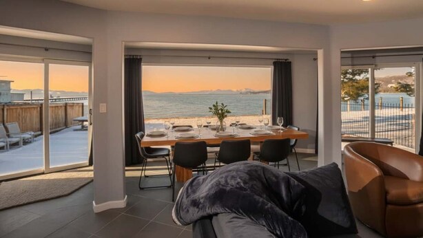 A dining area with a view of the sea, a large window, and a modern interior design. - Private Beach, Lakefront Home, Close to Everything (South Lake Tahoe)
