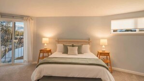 A bedroom with a bed, two bedside tables, a bench, a window with curtains, and a view of trees. - Private Beach, Lakefront Home, Close to Everything (South Lake Tahoe)