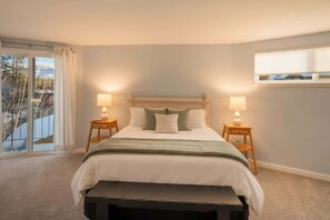 A bedroom with a bed, two bedside tables, a bench, a window with curtains, and a view of trees. - Private Beach, Lakefront Home, Close to Everything (South Lake Tahoe)