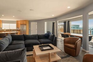 A modern living room with a sectional sofa, a coffee table, and a dining area with a view. - Private Beach, Lakefront Home, Close to Everything (South Lake Tahoe)