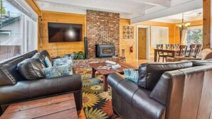 Una sala de estar con chimenea, sofás de cuero, un televisor y un comedor con sillas.