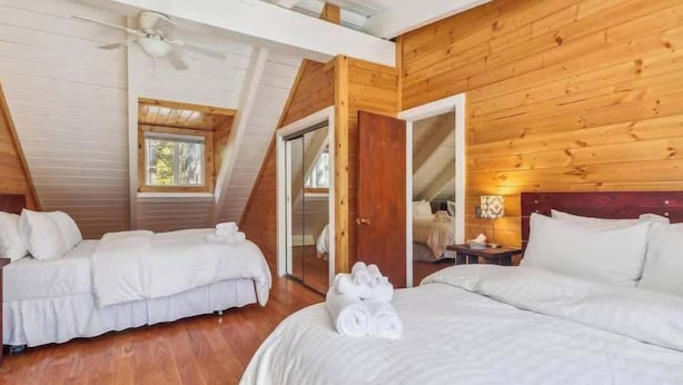Habitación con dos camas, ventilador de techo, paredes de madera y una ventana.