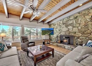 Ein gemütliches Wohnzimmer mit Steinwand, Kamin, Deckenventilator und großen Fenstern.