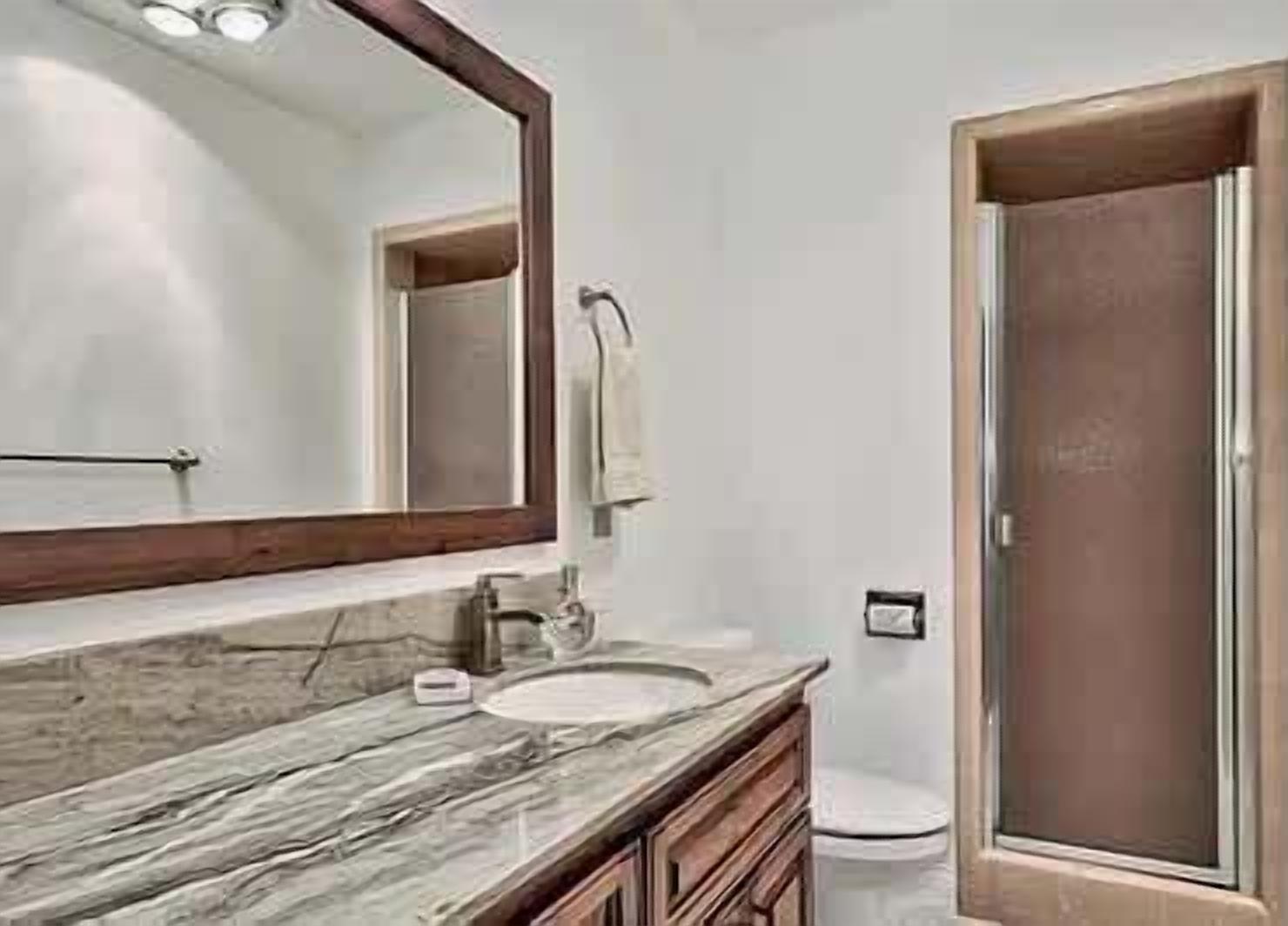 A bathroom with a marble countertop, a sink, a mirror, a towel rack, and a shower door.