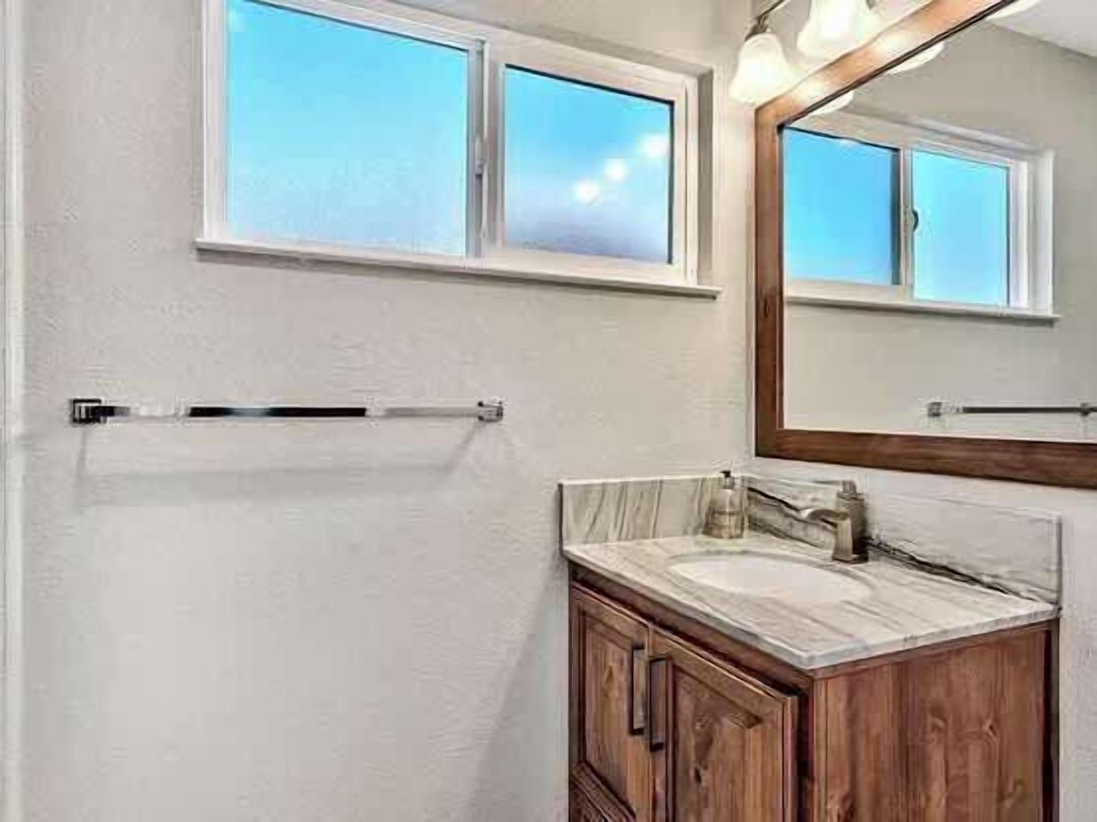 A bathroom with a window, a mirror, a towel rack, a sink, and wooden cabinets.