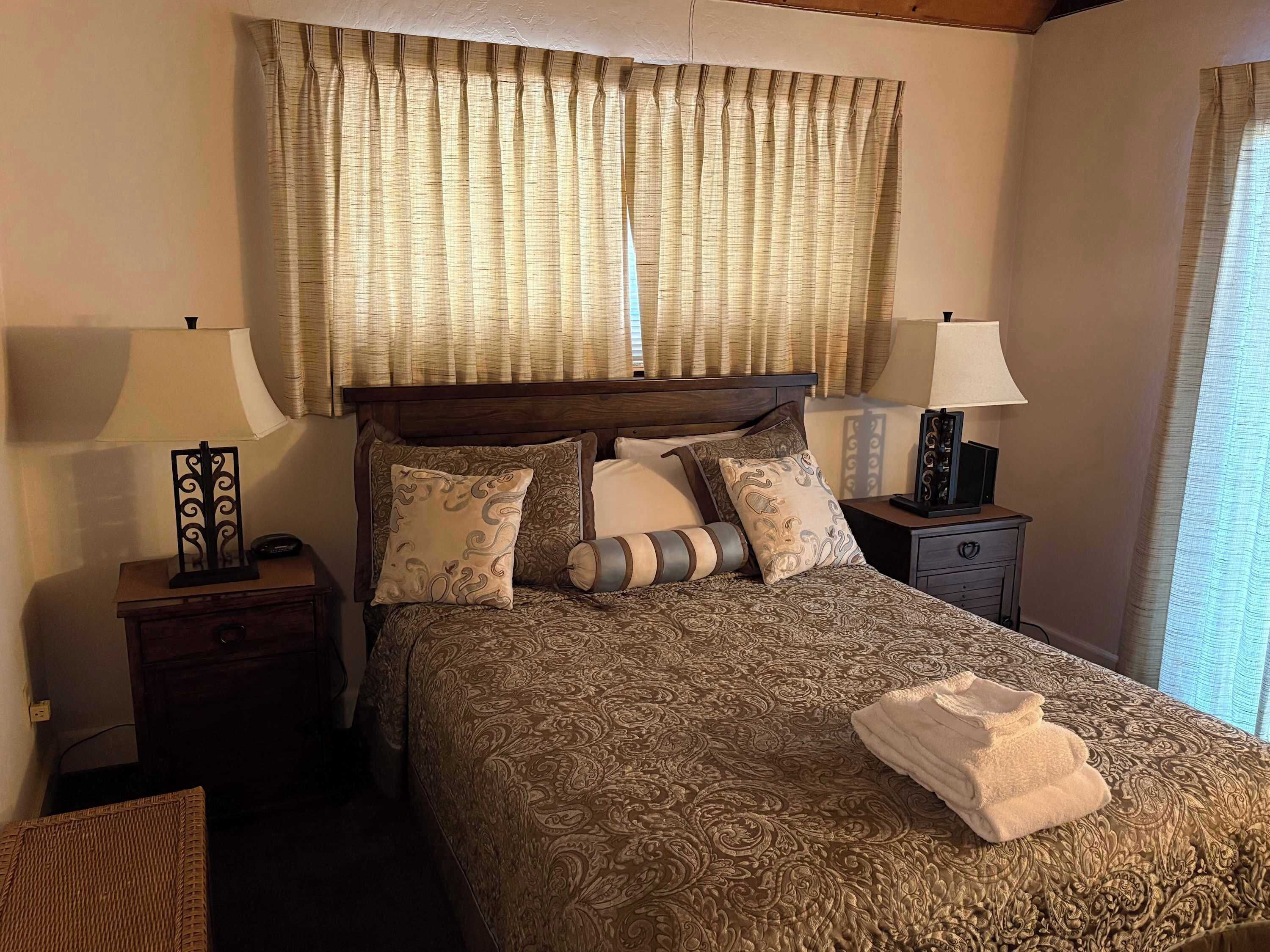 A hotel room with a large bed, two bedside tables, a lamp, and a window with curtains.