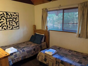 Ein Zimmer mit zwei Betten, einem hölzernen Kopfteil, einem Wandbild und einem Fenster mit Vorhängen.