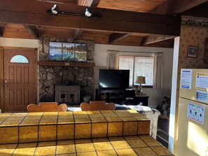 Ein gemütliches Wohnzimmer mit Kamin aus Stein, einem Fernseher und einem Essbereich mit einem gefliesten Tisch.