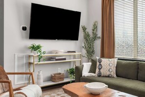 A living room with a flat-screen TV, a sofa, a wooden coffee table, and a bookshelf with decorative items. - The Wild Rose House - Rooftop Skyline + Sauna! (Nashville)