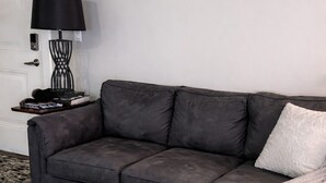 Ein dunkelgraues Sofa mit einer weißen Decke, ein brauner Hocker und eine schwarze Lampe auf einem Beistelltisch.