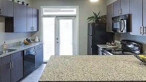 Eine moderne Küche mit dunklen Schränken, einer Arbeitsplatte aus Granit, einem Kühlschrank, einer Mikrowelle und einem Herd.