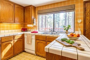 A kitchen with wooden cabinets, a red toaster, a sink, and a window with a view of trees. - Tahoe Cabin with Stone Fireplace, 2-Car Garage & Fenced Yard — Steps to the River (South Lake Tahoe)