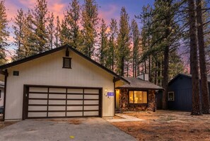 A single-story house with a garage, a stone fireplace, and a small shed in a forested area. - Tahoe Cabin with Stone Fireplace, 2-Car Garage & Fenced Yard — Steps to the River (South Lake Tahoe)