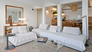 Una sala de estar moderna con un conjunto de sofá, una mesa de centro de vidrio y una cocina al fondo.