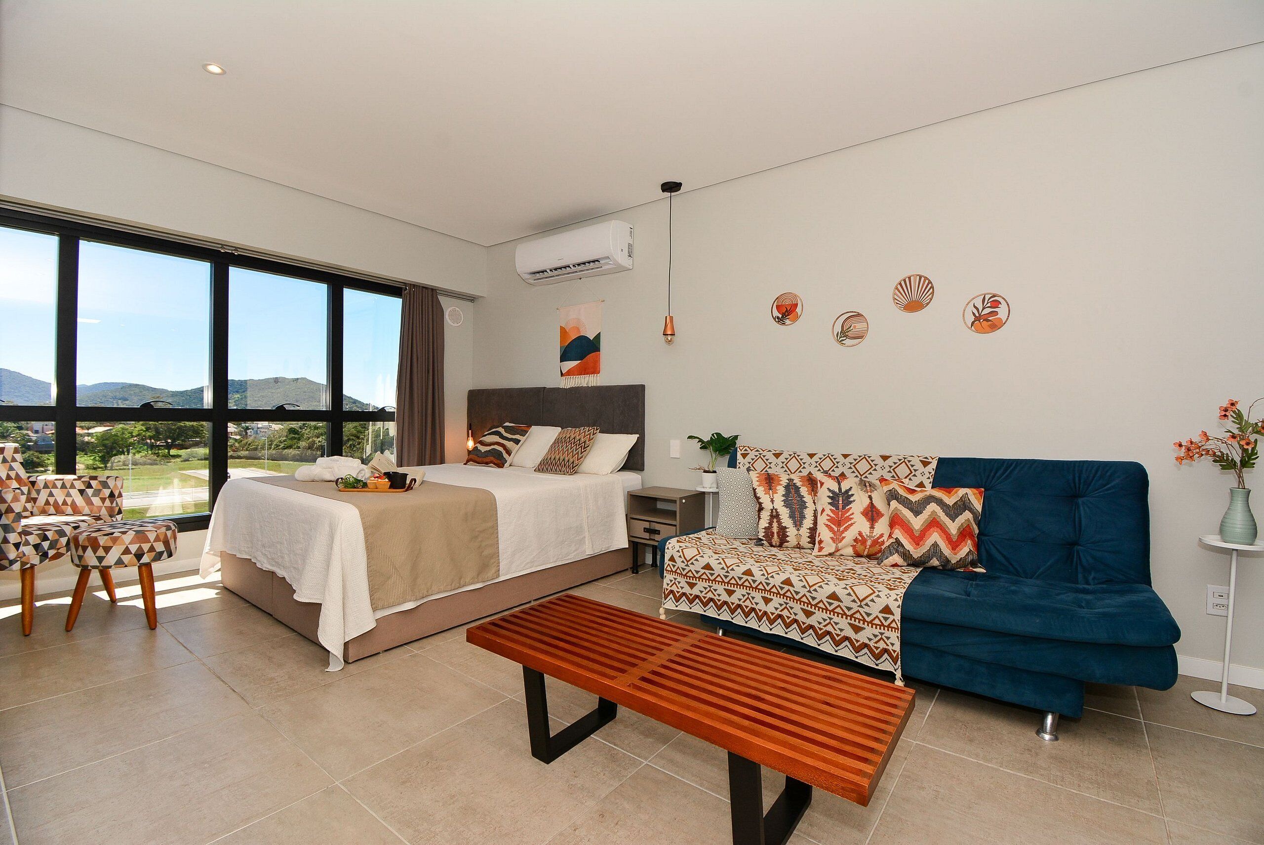 Una habitación de hotel moderna con una cama grande, un sofá, un banco y vistas al exterior.