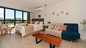 Una habitación de hotel moderna con una cama grande, un sofá, un banco y vistas al exterior.