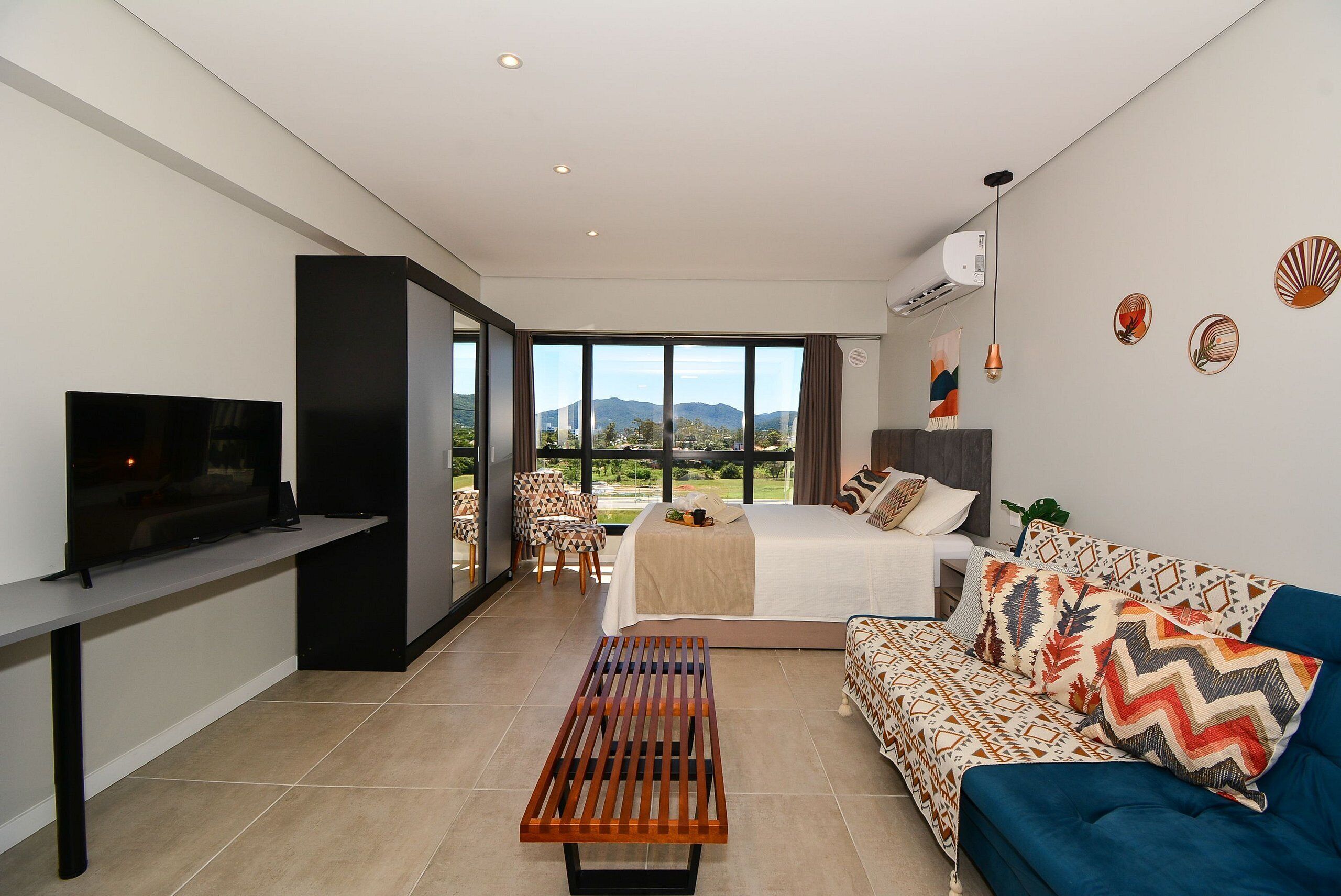 Quarto de hotel moderno com cama, sofá, televisão e vista para o exterior.