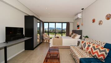 Quarto de hotel moderno com cama, sofá, televisão e vista para o exterior.
