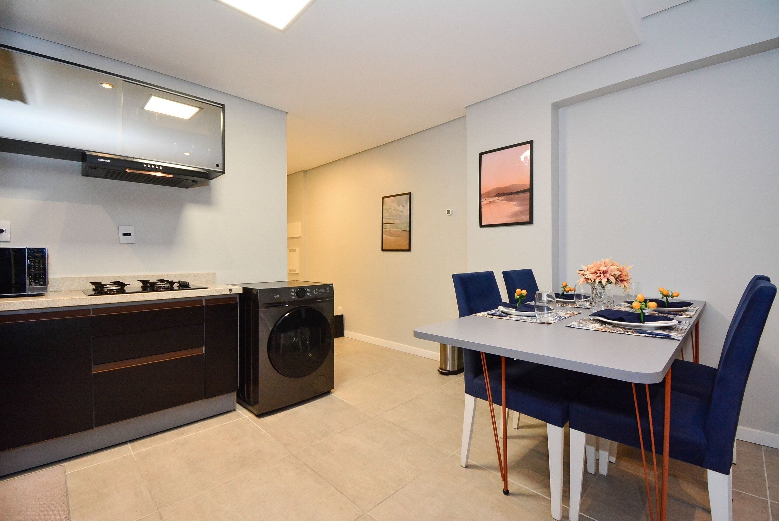 Una cocina moderna con lavadora integrada, un comedor con sillas azules y un cuadro en la pared.