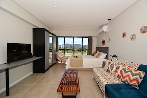 A modern hotel room with a bed, sofa, TV, and a view of the outdoors. - Studio Shopping OKA Floripa - SOK239 (Florianópolis)