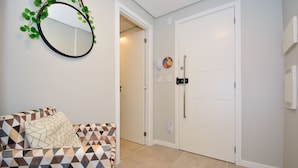 Una habitación con un sofá estampado, un espejo redondo con plantas, una puerta blanca y un teléfono fijado a la pared.