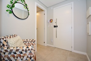 A room with a patterned sofa, a round mirror with greenery, a white door, and a wall-mounted phone. - Studio Shopping OKA Floripa - SOK239 (Florianópolis)