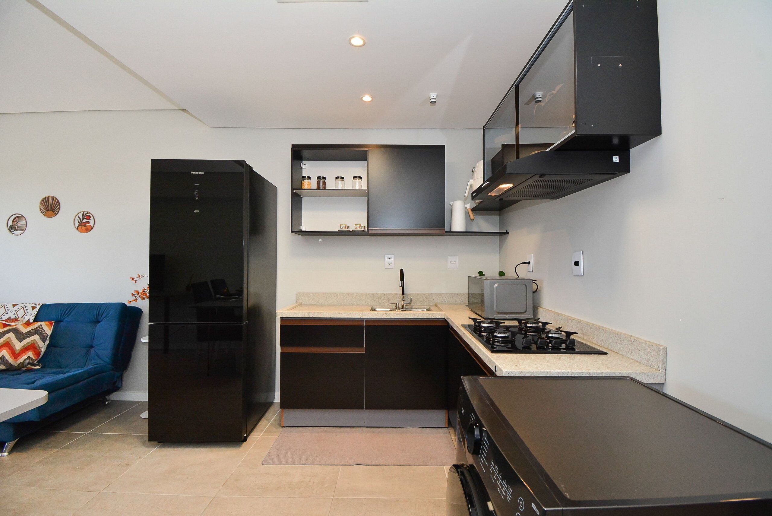 Cocina compacta con refrigerador, microondas, estufa y un estante empotrado sobre el lavamanos.