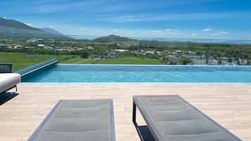 Vista da piscina com duas espreguiçadeiras, céu claro e paisagem distante.
