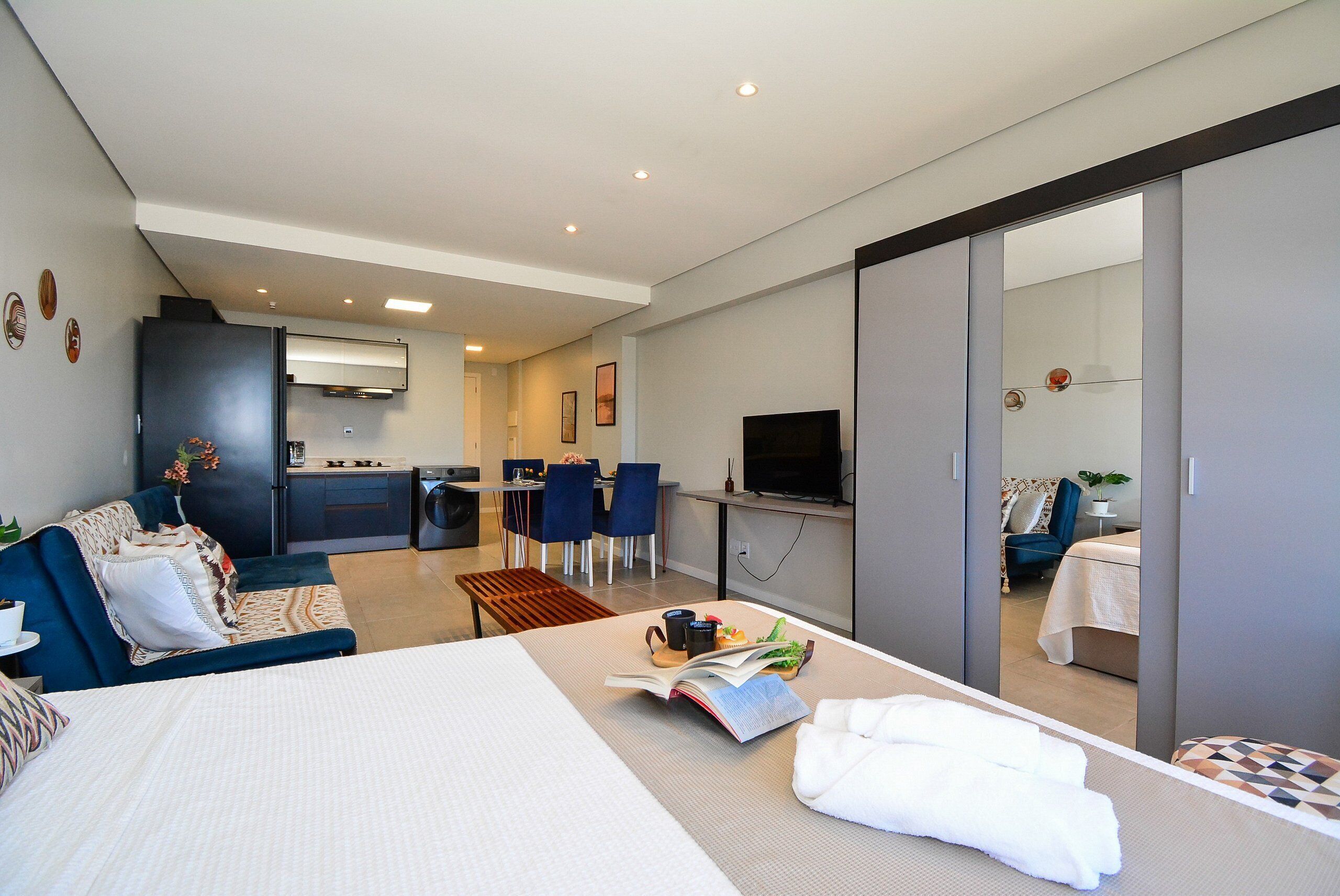 Quarto de hotel moderno com cama, sofá, área de refeições e cozinha.