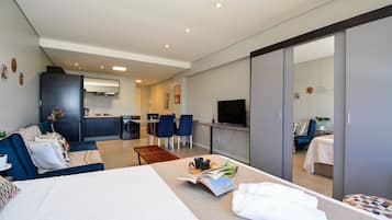 Quarto de hotel moderno com cama, sofá, área de refeições e cozinha.